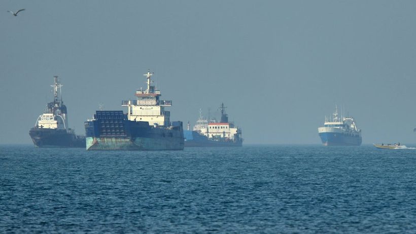 Cargo ships, including bulk carriers and general cargo vessels, sit at anchor offshore as a small motorboat passes in the foreground, in the Strait of Hormuz off Bandar Abbas, Iran, Monday, May 4 , 2026.(Amirhosein Khorgooi/ISNA via AP) XEM103